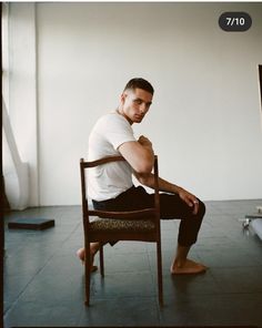 a man sitting on top of a wooden chair in front of a white wall and floor