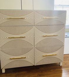 a white cabinet with gold lines painted on the front and sides, along with a wooden floor