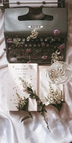 an old fashioned typewriter with flowers and a book on the bed next to it