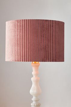 a white lamp with a pink shade on top of it and a wooden table underneath