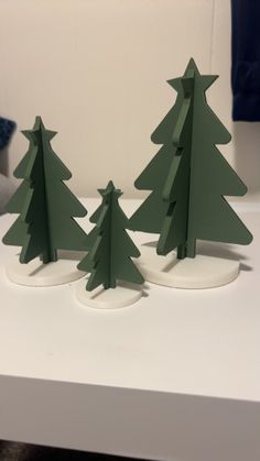 three small green trees sitting on top of a white table