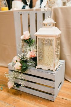 a wooden crate with flowers and a lantern on top is sitting on the floor in front of a table