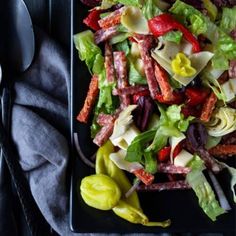 a black plate topped with salad next to a fork and knife on top of a table