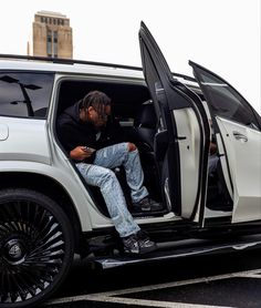 a man sitting in the open door of a white suv while looking at his cell phone