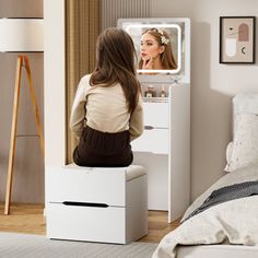 a woman is looking at her reflection in the mirror while sitting on a white vanity