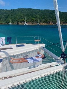 a man laying on the deck of a sailboat in the blue water with mountains in the background