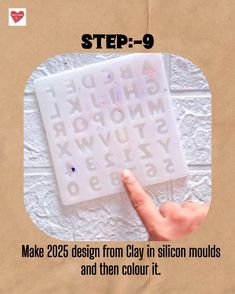 a hand is pointing at the letter stencil on a piece of paper that says, make 205 design from clay in stiln moulds and then color it