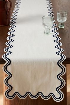 a long table with two glasses on it and a white table runner that has black scalloped edges