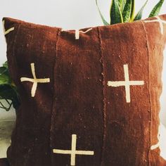 a brown pillow with crosses on it sitting next to a potted plant in the corner