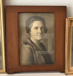 an old photo of a woman in a brown frame next to two framed pictures on a wall