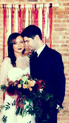 a bride and groom standing next to each other in front of a red brick wall