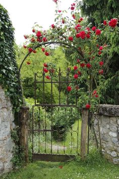 an old iron gate with roses growing on it and stone walls surrounding the entrance to a garden