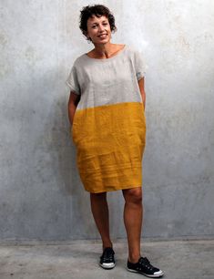 a woman standing in front of a wall wearing a yellow and grey dress with black shoes