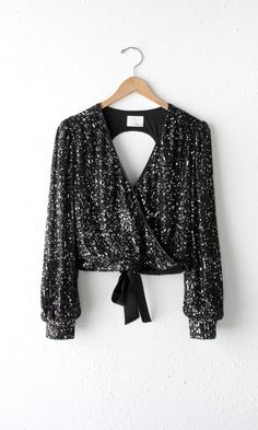 This long sleeve sequin top will make you look and feel powerful. It has a v-neckline and an open back. The shirt is secured with a tie in the back while cinching the waist. Fully lined. Sequin top Open back Long sleeves V-neck Satin tie Cuffed Lined Self: 100% Polyester Lining: 100% Polyester Length: 18" Chest: 17 1/4" Hand wash in cold water. Lay flat to dry. Model is wearing a size small Style #: G2210T6639 Sparkly Shirt Sequin Top, Faux Leather Leggings With Sequined Top, Luxury Sequin V-neck Tops, Luxury Party Blouse With Sequins, Luxury Georgette Tops With Sequins, Luxury Black Blouse With Sequins, Luxury Black Blouse Piece With Sequins, Luxury Sequined Embroidered Top For Party, Luxury Sequined Party Top