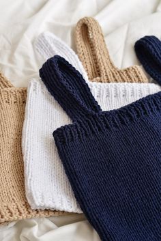 two knitted sweaters laying next to each other on top of a white sheet