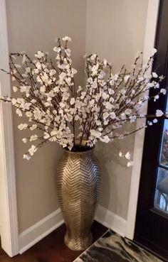 a vase filled with white flowers sitting on top of a wooden floor next to a door