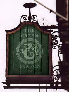 the green dragon sign is hanging on the side of a building in front of a light pole