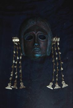 an ancient mask with gold chains hanging from it's face and eyes, in the dark