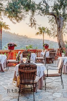 an outdoor dining area with tables and chairs set up for dinner under a large tree