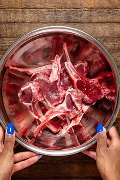 two hands holding a metal bowl filled with raw meat