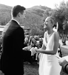 a bride and groom standing in front of an audience at a wedding ceremony, with one holding the other's hand