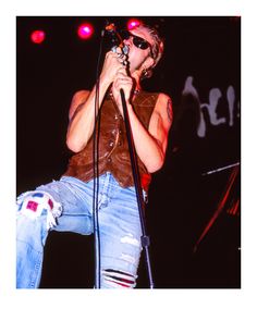 a man standing on stage holding a microphone in his right hand and wearing ripped jeans