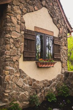 a window with shutters and flower boxes on the outside of an old stone building