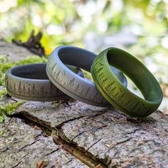 two green wedding rings sitting on top of a tree branch in the woods with writing on them