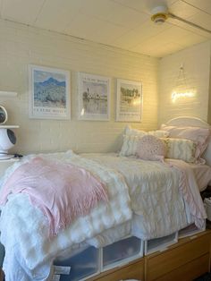 a white bed with pink comforter in a bedroom next to two pictures on the wall