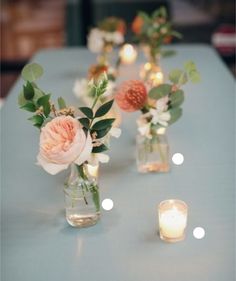 several vases with flowers and candles on a blue table cloth covered table in an indoor setting