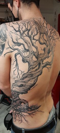 the back of a man with a tree tattoo on his upper and lower half body