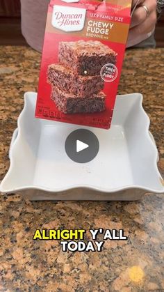 someone is holding up a box of fudge cake on a white plate in front of a granite counter top