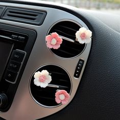 three pink and white flowers are placed on the dashboard of a car's dash board