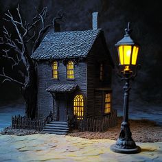 a miniature house with a light on in front of it and a tree next to it