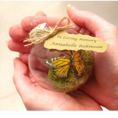 a hand holding a small glass ornament with a butterfly on it and a tag that says in loving memory