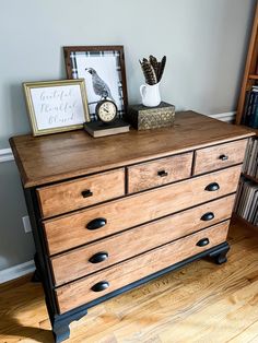 a wooden dresser with two pictures and a clock on it's top, in front of a bookshelf