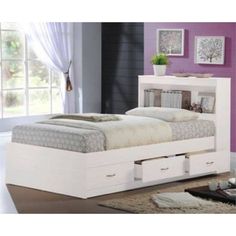 a white bed with drawers underneath it in a purple and white room, next to a window