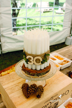 a birthday cake with candles and pine cones on a table in front of a tent