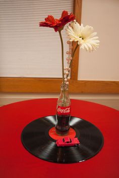 a coca cola bottle with flowers in it on top of a vinyl record album table