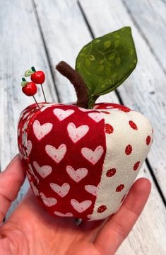 a hand holding an apple with hearts and a green leaf on the top of it