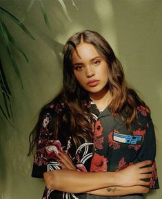 a woman standing in front of a green wall with her arms crossed and looking at the camera