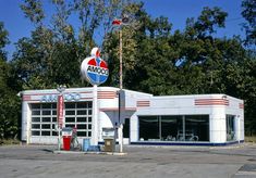 an old gas station sits empty in the middle of a parking lot next to some trees