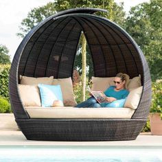 a woman laying on top of a bed next to a pool with a book in her lap