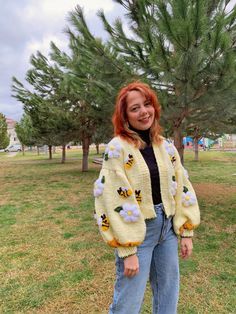 a woman standing in the grass wearing a bee sweater