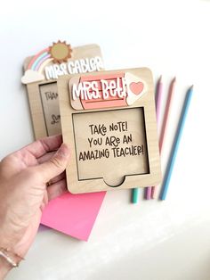 a person holding up a wooden frame with writing on it and some colored pencils