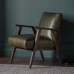 a green leather chair sitting on top of a wooden floor next to a rug and wall