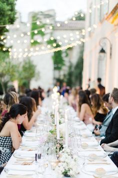 a long table is set with white plates and place settings for an elegant dinner party