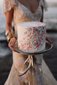 a woman holding a white cake with pink, blue and red sprinkles