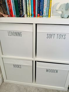 a white bookcase with books and toys on top of it in front of a wall