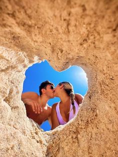 a man and woman kissing in the sand with a heart shaped hole on their face